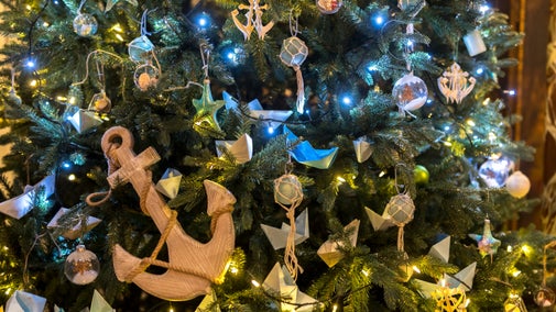 Close up of Christmas tree decorated in a nautical theme with a large wooden anchor in the foreground